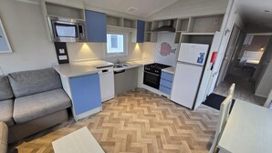 Une cuisine compacte équipée d’un four à micro-ondes, d’une cuisinière et d’un réfrigérateur. Le coin salon comprend un canapé et une petite table.
