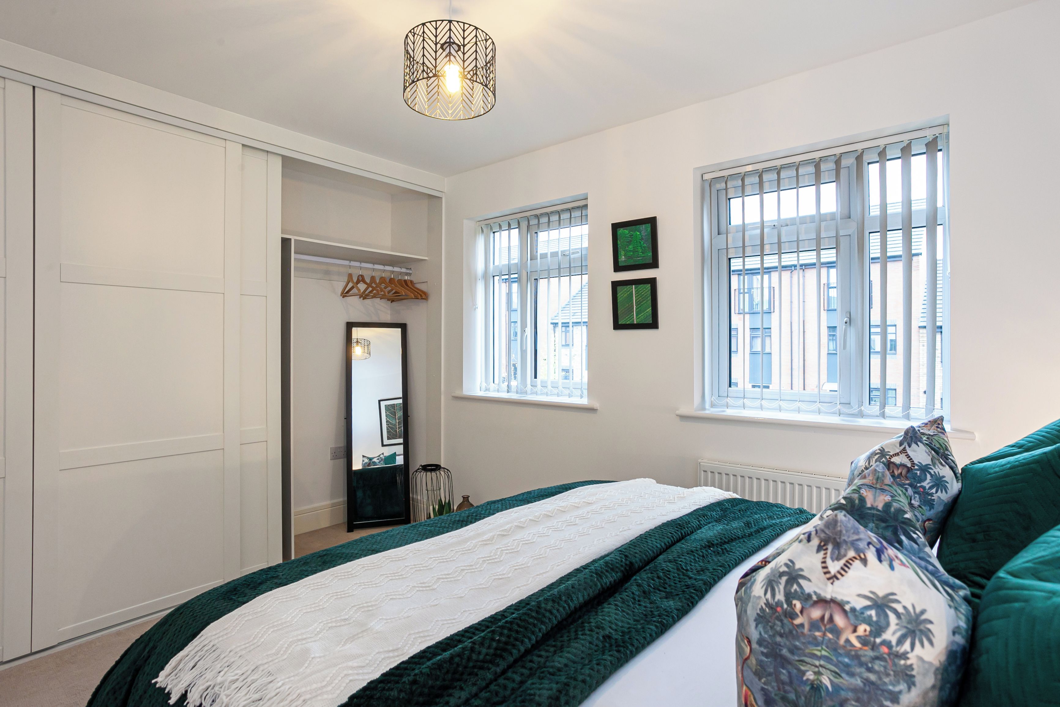 A bedroom with a bed, a wardrobe, a mirror, and two windows.