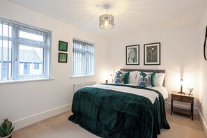 Une chambre à coucher avec un grand lit, une table de chevet, une lampe et une fenêtre avec des stores.