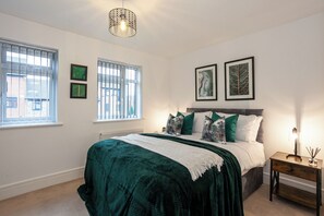 A bedroom with a bed, two windows, a radiator, and wall-mounted artwork.