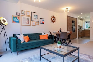 Un salon moderne avec un canapé vert, une table basse en verre et un coin repas comprenant une table et des chaises.