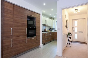Une cuisine moderne avec des meubles en bois, un four à micro-ondes, un four traditionnel et un petit coin repas avec une table et des chaises.