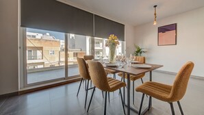 Ruokailutila, jossa on suuri ikkuna, neljälle katettu ruokapöytä ja maljakko täynnä kukkia.