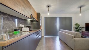 Een moderne keuken met een marmeren spatwand, houten kastjes en een ingebouwde oven. Er is een zithoek met een bank en een televisie.