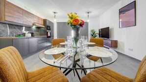 Een moderne eethoek met een glazen tafel, twee stoelen en een bloemenvaas.
