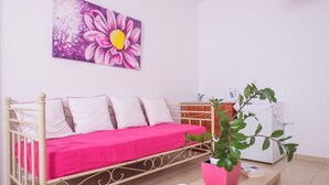 Una habitación con una cama, una planta en maceta, un florero blanco y un cuadro en la pared.