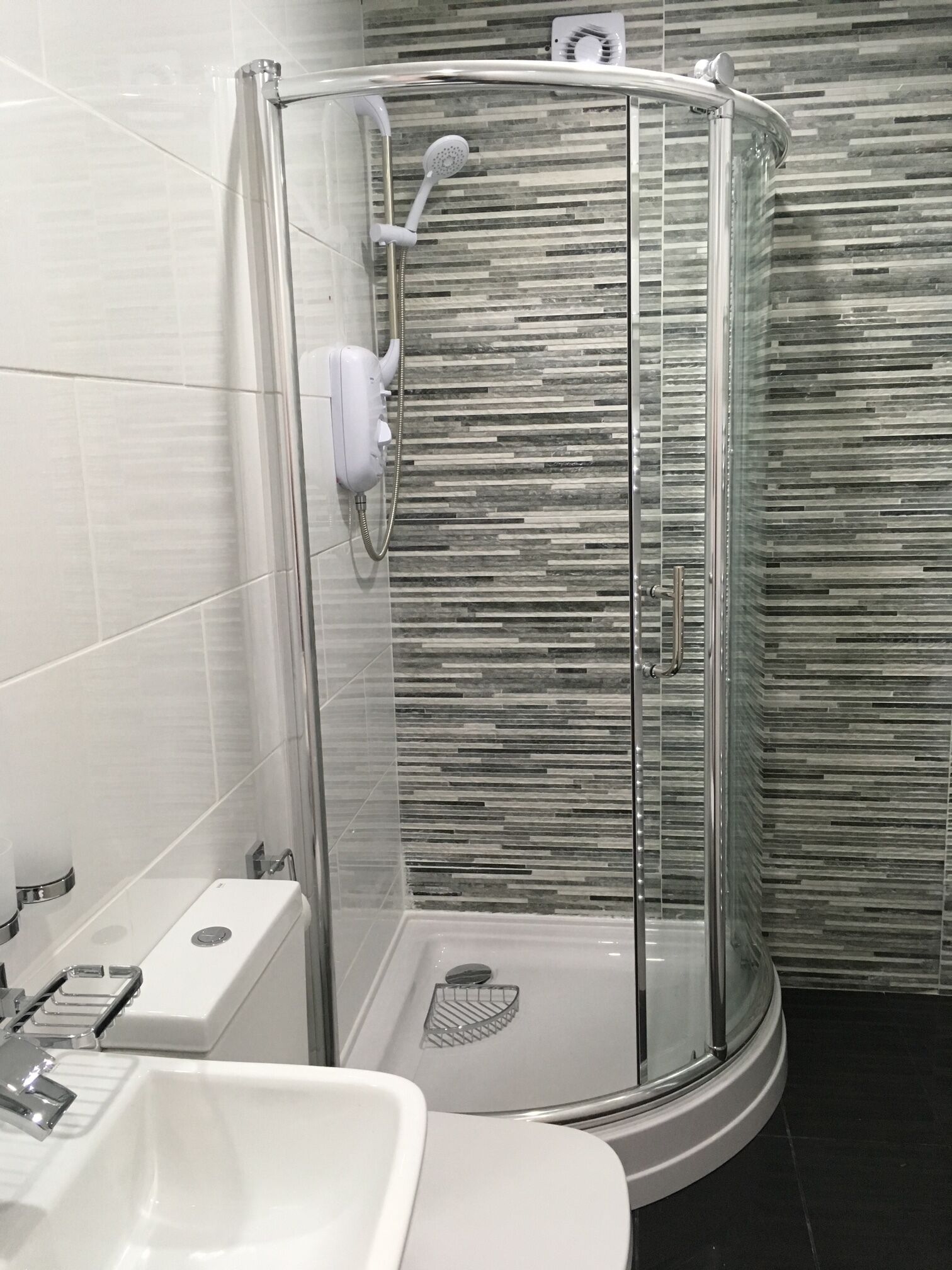 Ein modernes Badezimmer mit einer Duschkabine aus Glas, einem weißen Waschbecken und einem Fliesenboden.