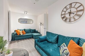 Ein modernes Wohnzimmer mit Türkis-Farbenen Sofas, einer großen Wanduhr und einem minimalistischen Design.