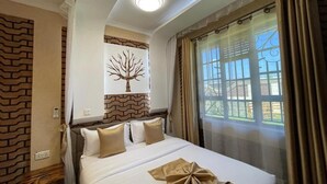 Ein Hotelzimmer mit Bett, einer Wanddekoration mit Baummotiv, einem Fenster mit Vorhängen und einer Deckenleuchte.
