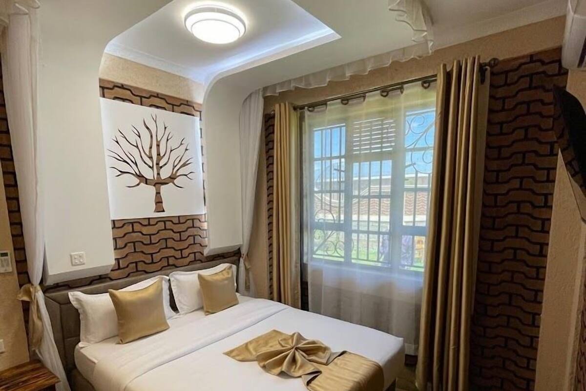 Een hotelkamer met een groot bed, een plafondlamp, een raam met gordijnen en een kunstwerk van een boom aan de muur.