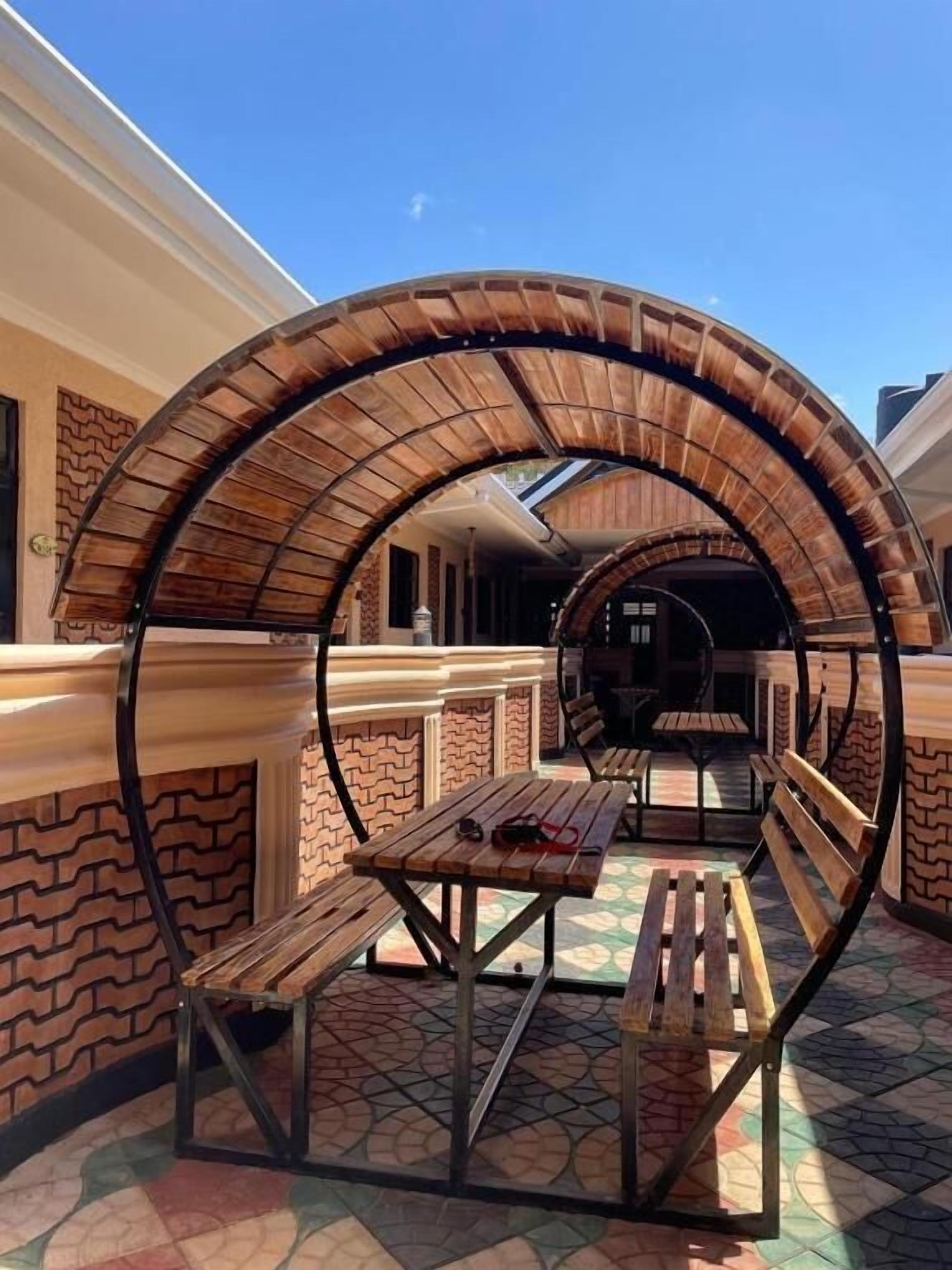 Un espace extérieur aménagé avec des bancs et des tables en bois, un mur de briques et un ciel d’un bleu limpide.