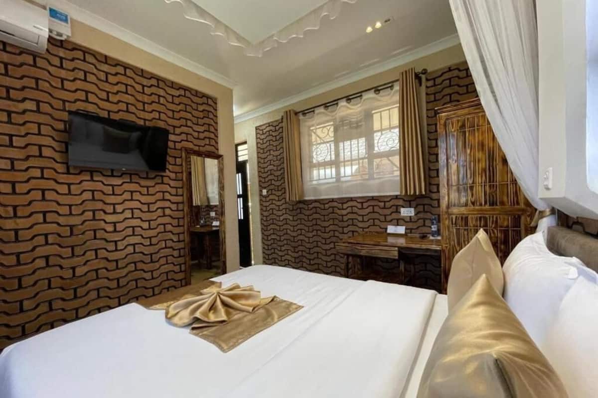 Een hotelkamer met een wand met baksteenmotief, een flatscreen televisie boven het bed, een bureau met stoel, en een raam met gordijnen.