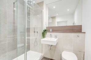 A modern bathroom with a glass shower enclosure, a white sink, and a wooden vanity. - Battersea 2-Bed Apt, Sleeps 4 with WiFi (London)