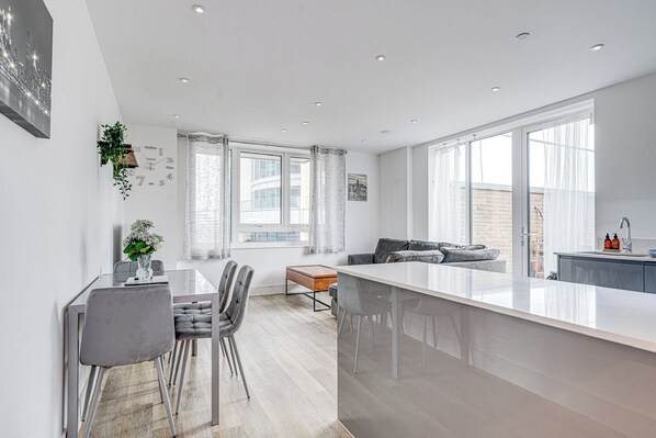 A modern kitchen with a central island, a dining area with chairs, and a sofa. - Battersea 2-Bed Apt, Sleeps 4 with WiFi (London)