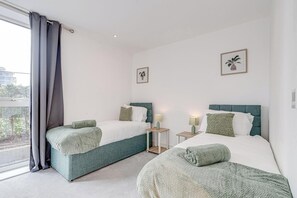 A hotel room with two beds, a balcony with curtains, and two framed pictures on the walls. - Battersea 2-Bed Apt, Sleeps 4 with WiFi (London)