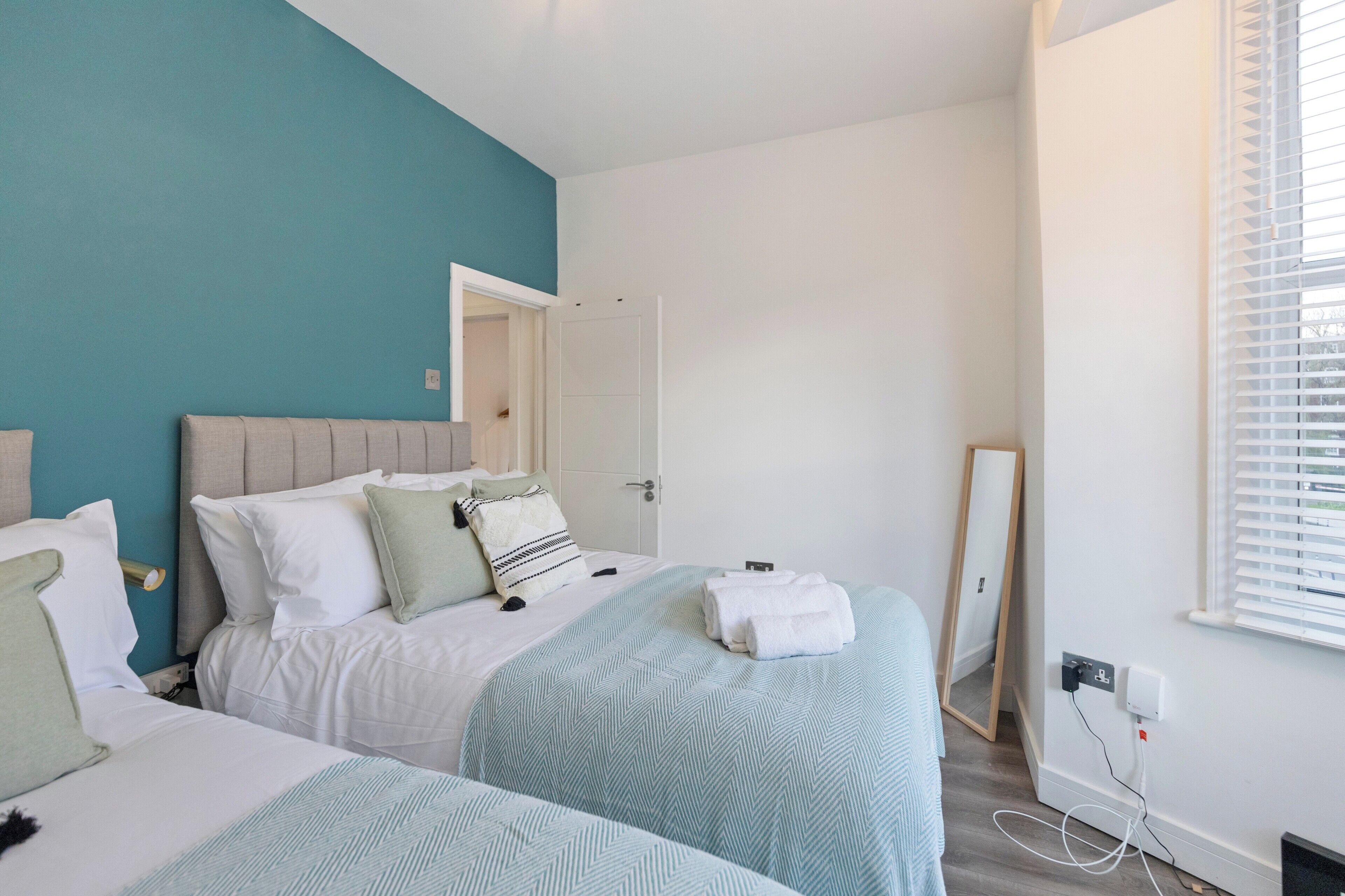 Un dormitorio con dos camas, una pared de acento color verde azulado y un espejo grande.