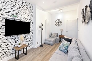 A modern living room with a flat-screen TV, a patterned wall, a grey sofa, and a wooden coffee table. - Apartment - Sleeps 11 - Hampstead HighStreet 5mins (London)