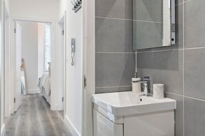 A modern bathroom with a white sink, grey tiles, and a mirror. - Apartment - Sleeps 11 - Hampstead HighStreet 5mins (London)
