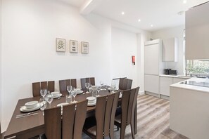 A modern dining room with a rectangular table set for six, surrounded by six chairs. There are framed botanical prints on the wall above the table. - Apartment - Sleeps 11 - Hampstead HighStreet 5mins (London)