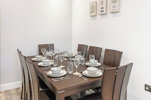 A dining table set for six with six chairs, white plates, bowls, cutlery, and wine glasses. - Apartment - Sleeps 11 - Hampstead HighStreet 5mins (London)