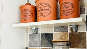 Three terracotta containers labeled 'SUGAR', 'MUSHROOMS', and 'TEA' on a white shelf against a tiled wall. - Ulverston Cozy Cottage Retreat (Ulverston)
