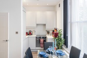 A modern kitchen with white cabinets, a built-in oven, and a dining area with blue plates and candles. - Charming London Apartment in Central London (London)