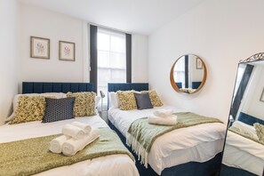 A hotel room with two beds, a large mirror, and a window with curtains. - Charming London Apartment in Central London (London)