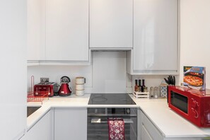A modern kitchen with white cabinets, a red microwave, a gas stove, and a built-in oven. - Charming London Apartment in Central London (London)