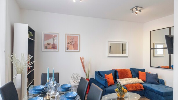 Ett modernt vardagsrum med en blå soffa, ett matbord dukat med blå tallrikar och ett soffbord i glas.