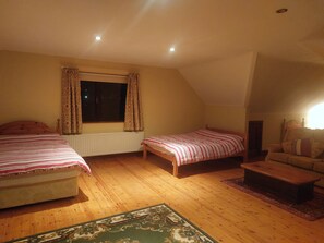Un dormitorio con dos camas, una ventana con cortinas, un radiador, suelo de madera y un sofá.