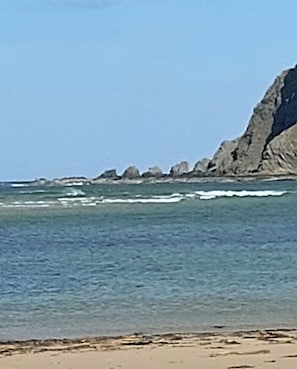 A beach with clear water, rocky cliffs, and a sandy shore.