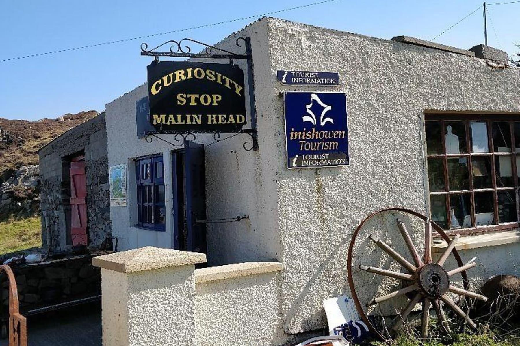 A small building with a sign reading "Curiosity Stop Malin Head" and another sign for "Inishowen Tourism."