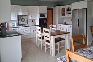 A kitchen with white cabinets, a dining table with chairs, a microwave, a stove, and a refrigerator.