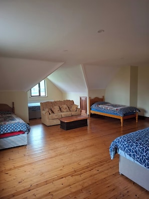 A room with a sloped ceiling, wooden flooring, a sofa, a bed, and a small table.