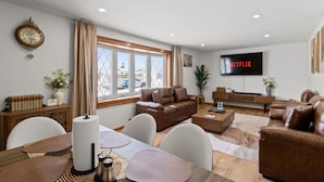 En moderne stue med en brun lædersofa, et træsofabord og et fladskærms-tv, der viser 'NETFLIX'.