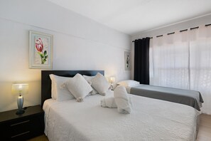 Une chambre d’hôtel avec deux lits, du linge de lit blanc, une table de chevet avec une lampe et des œuvres d’art encadrées accrochées au mur.