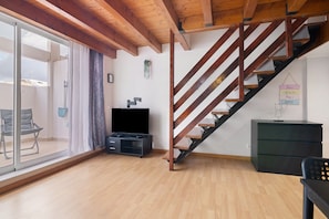 Un salon avec un escalier en bois, un téléviseur à écran plat et une porte vitrée donnant sur un espace extérieur.