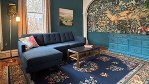 Una stanza con un divano blu scuro, un tavolino, un tappeto decorato, un armadietto blu e un grande murale floreale sulla parete.