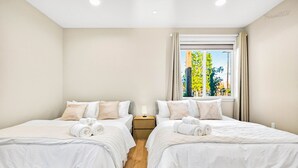 Quarto de hotel com duas camas, uma mesa de cabeceira e uma janela com vista para áreas verdes.