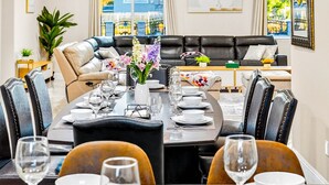 A dining area with a long table set for a meal, surrounded by chairs. There is a sofa and a coffee table in the background. - Spacious 9BR Home + Parking + Near DTLA #TravelSGV (Avocado Heights)