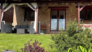 A stone building with a covered patio area, outdoor furniture, and a well-maintained lawn.