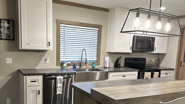 Una cocina moderna con armarios blancos, un refrigerador de acero inoxidable, un microondas integrado y una isla de madera con una silla.