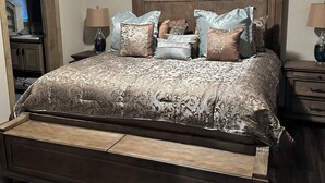 Un dormitorio con una cama grande, cabecera de madera y varios almohadones. Hay dos mesitas de noche con lámparas.