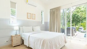 Een slaapkamer met een groot bed, een nachtkastje, een wandairconditioner en uitzicht op een buitengebied met een zwembad en ligbedden.