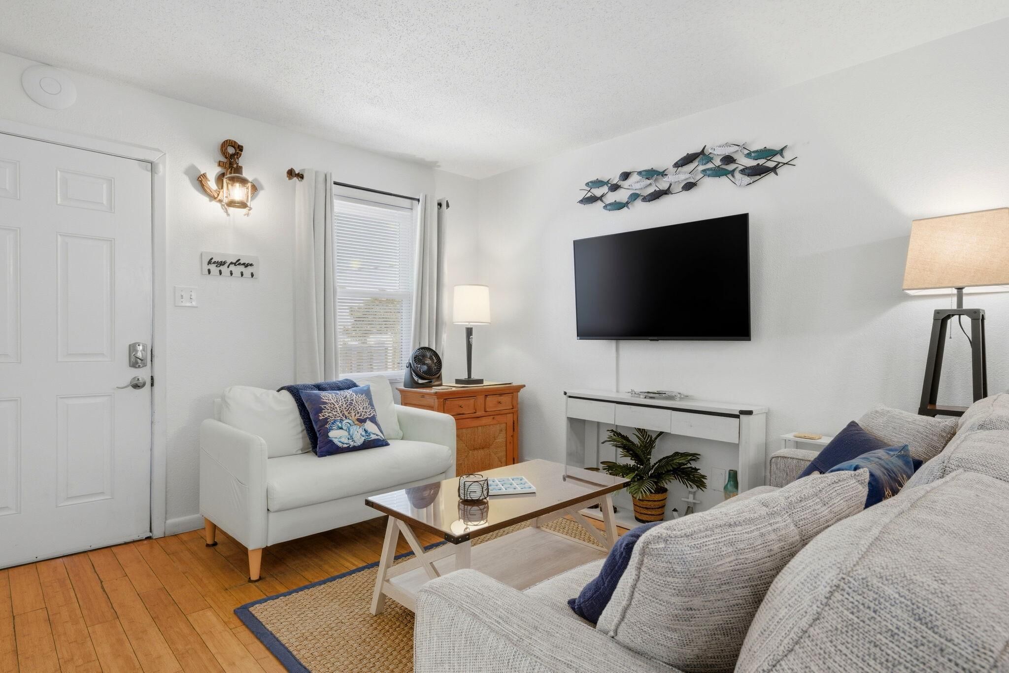 Una sala de estar con un sofá blanco, una mesa de centro, un televisor y una lámpara.