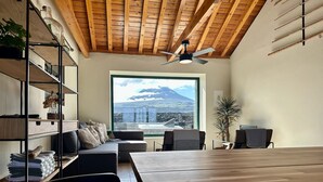 A modern room with a wooden ceiling, a large window with a mountain view, a dining table, and a seating area with a sofa and chairs.