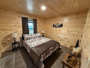 Une chambre dans une cabane en bois, comprenant un lit, deux tables de chevet, une chaise, une fenêtre avec des rideaux et un élément décoratif mural.