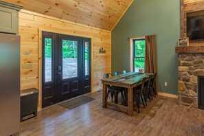 Un interior de madera con una mesa de comedor, sillas, una chimenea de piedra y una zona de cocina.