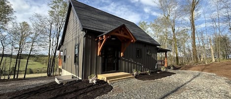 A rustic cabin with a sloped roof, wooden porch, and a gravel driveway.