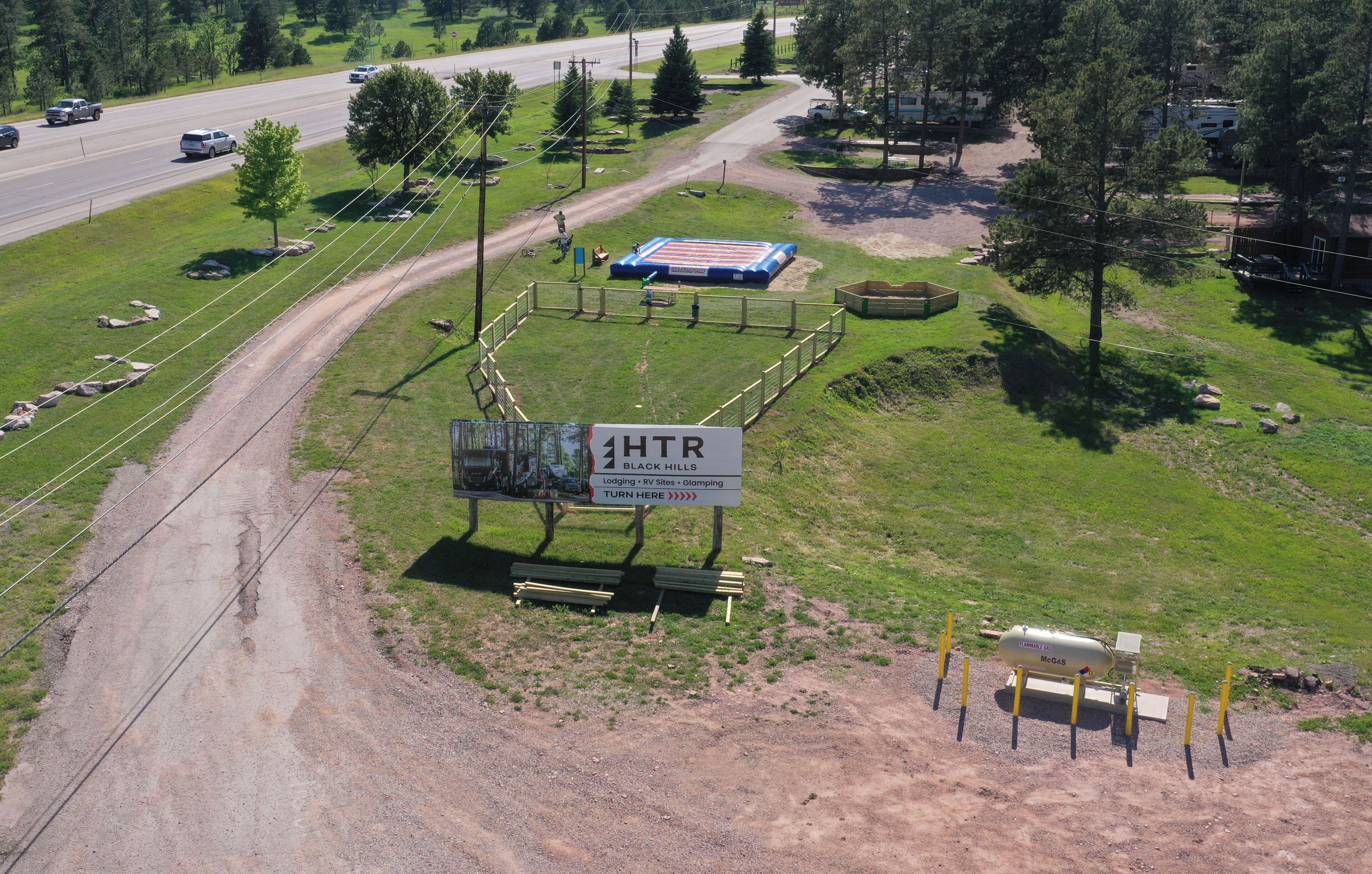 A road with a dirt path, a fenced area with a blue structure, and a sign for Black Hills RV sites.